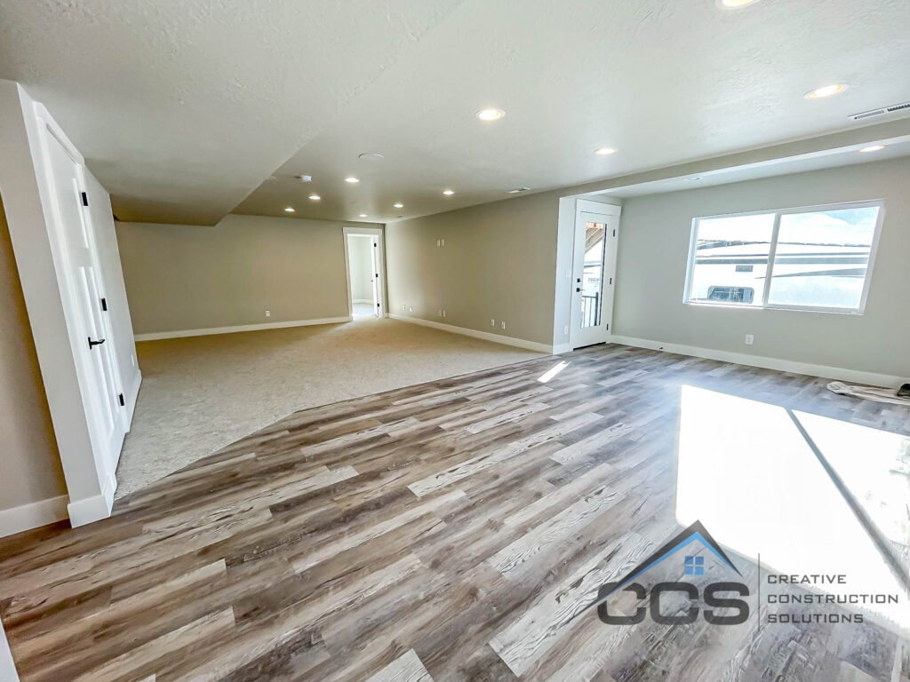 An image of a finished basement in Utah. A bright space with neutral colors. It is unfurnished. A logo for CCS Creative Construction Solutions is in the right-hand corner.
