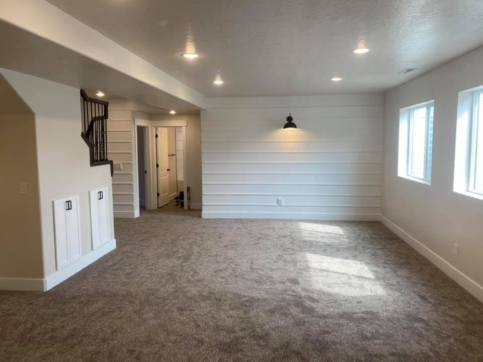 Empty basement room with carpeted floor, white shiplap walls, recessed lighting, and two windows.