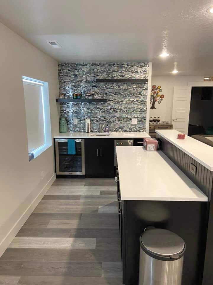 A modern kitchen with mosaic backsplash, white counter, and gray flooring.